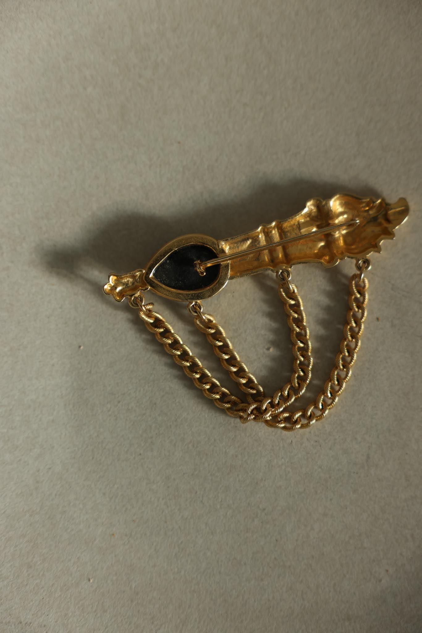 Matte Gold-Tone Draped Chain Brooch with Black Teardrop Center