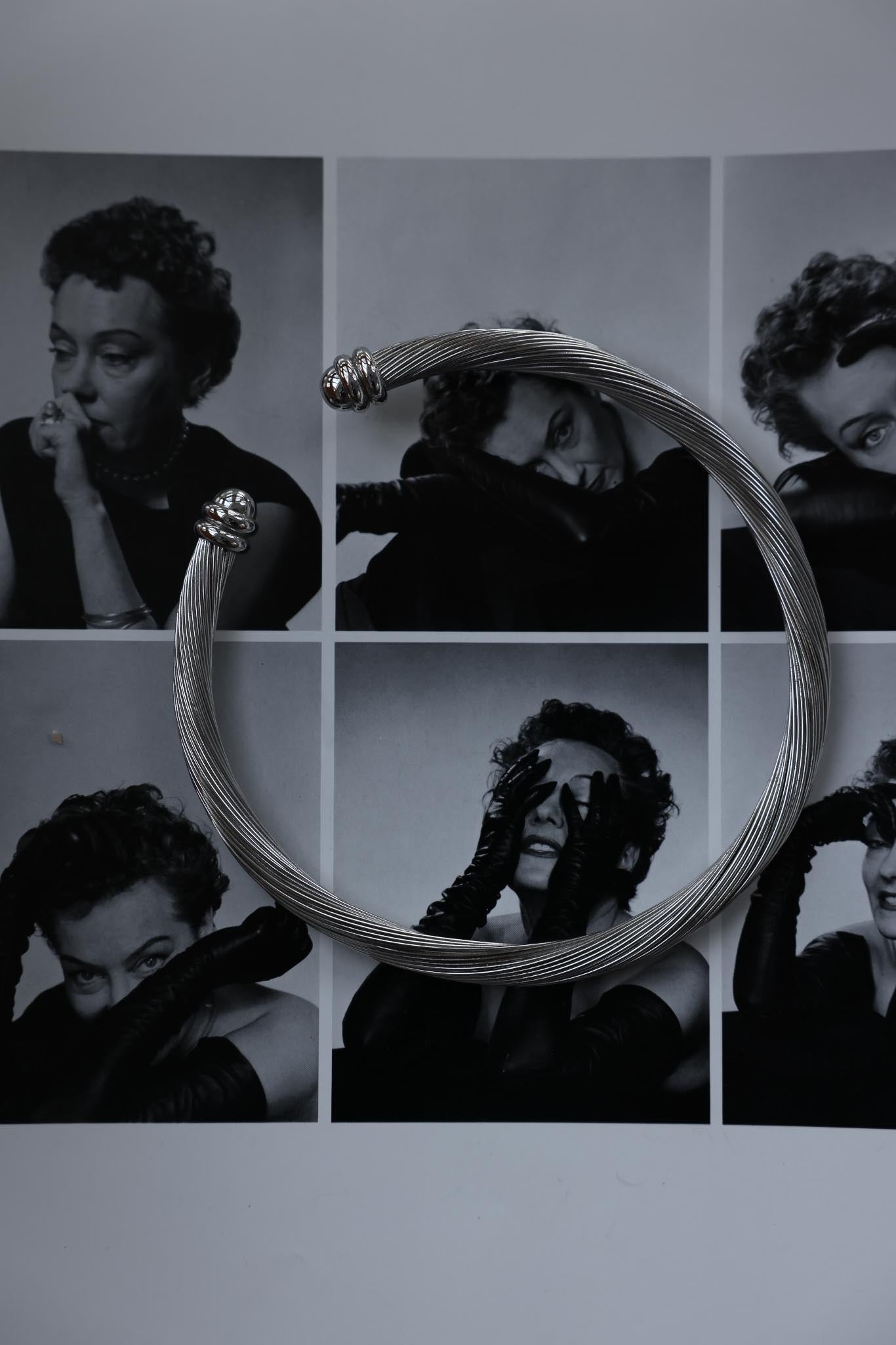 Vintage silver-tone collar necklace with a twisted design and decorative endcaps, displayed against a black-and-white photo collage background.