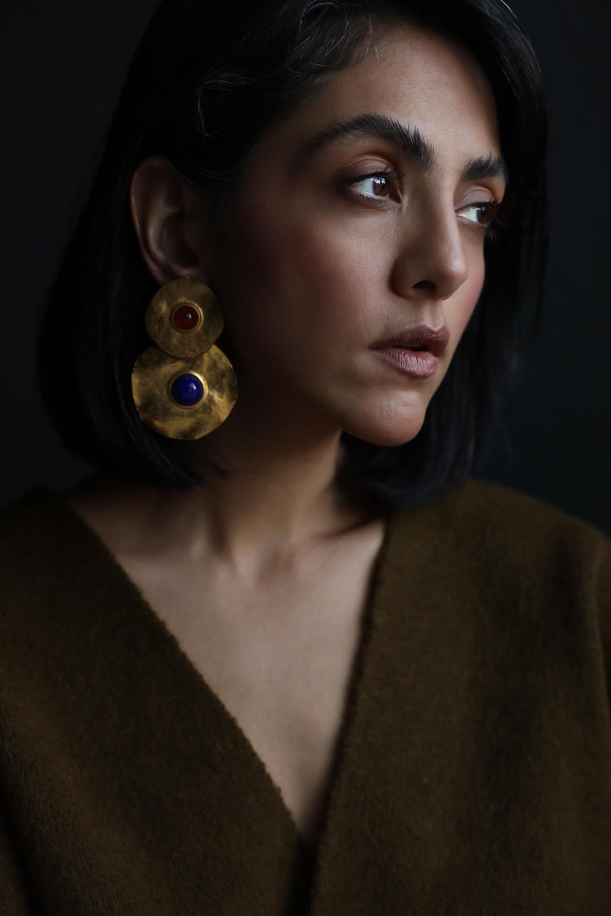 Close-up of a hammered gold disc clip-on earring with a blue glass center