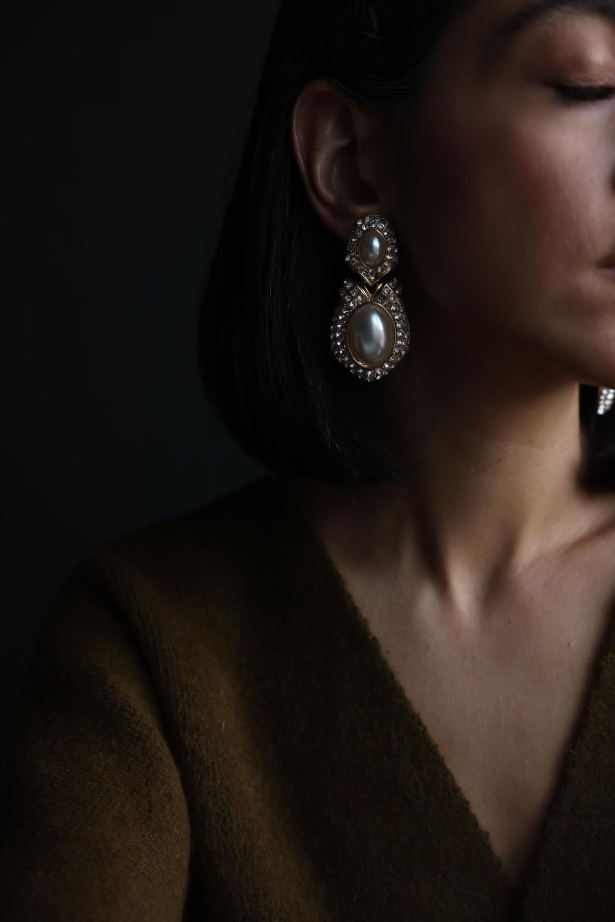 Faux pearl rhinestone drop earring worn with a brown V-neck sweater