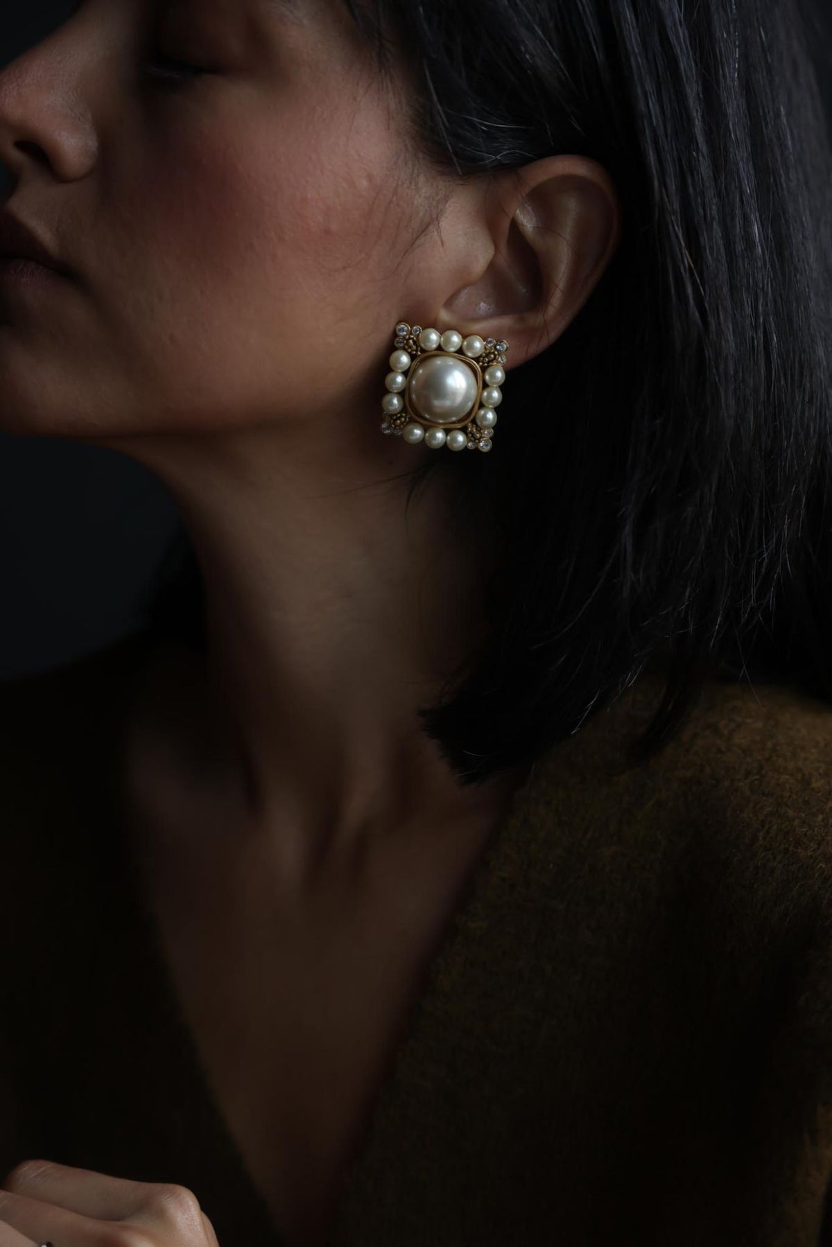 Woman wearing a square gold tone faux pearl clip-on earring, side profile
