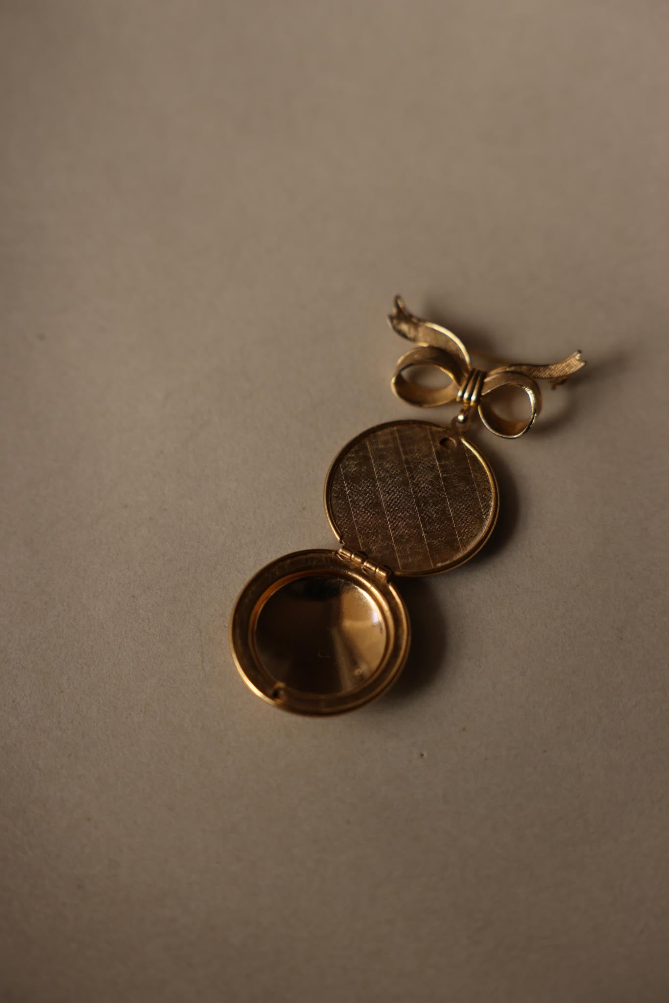 Vintage gold-tone photo locket brooch with engraved floral details and bow design