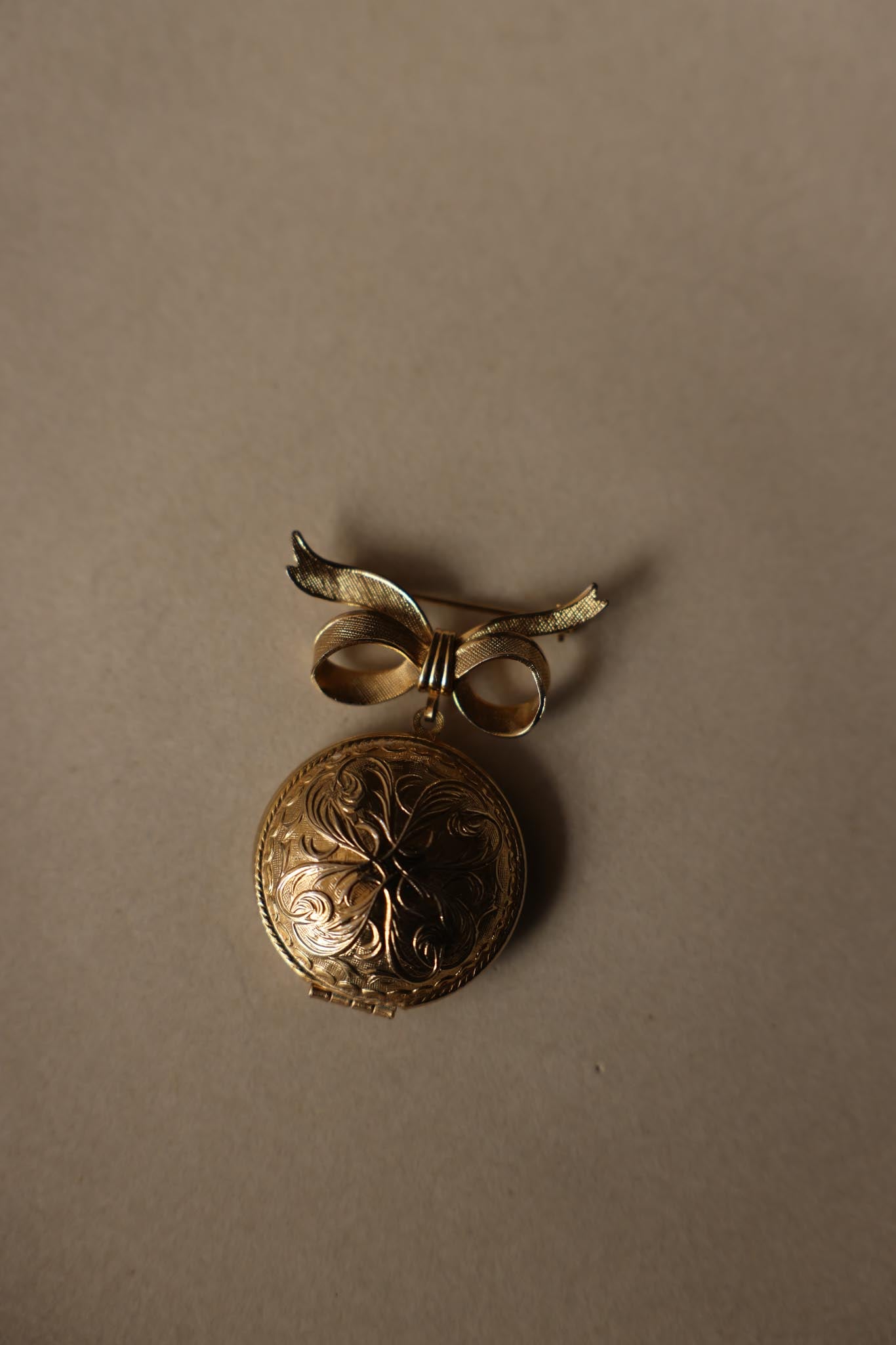 Vintage gold-tone photo locket brooch with engraved floral details and bow design