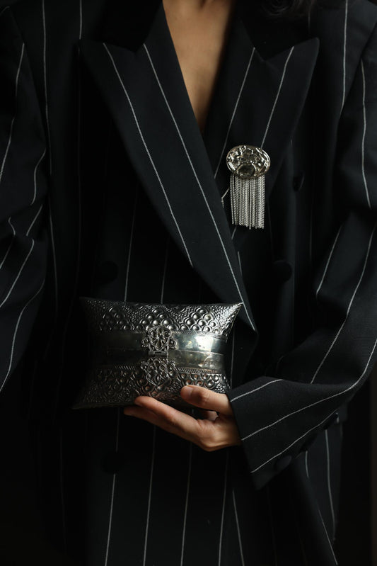 Woman in a pinstripe blazer holding an embossed silver tone pillow clutch