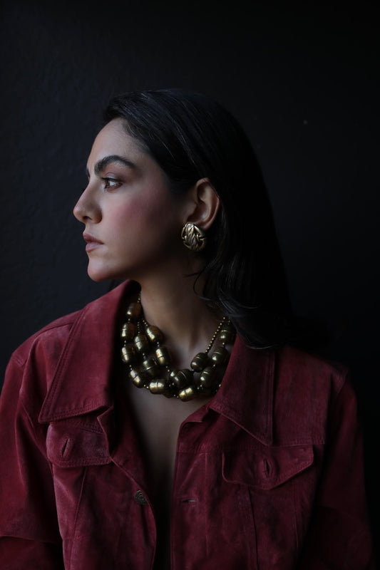 Styled look featuring the Braided Charm clip-on earrings paired with layered brass necklaces and a red suede jacket.