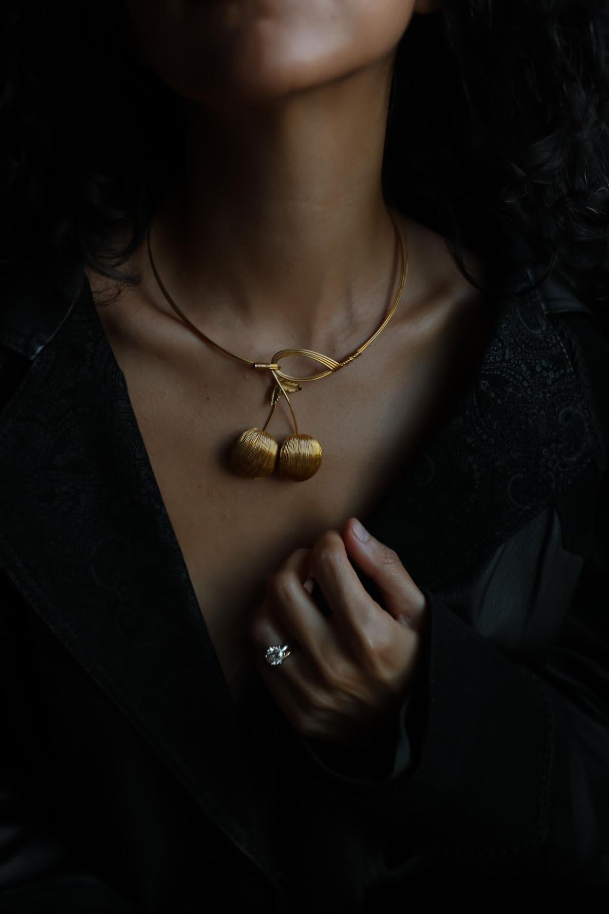 Gold tone cherry collar necklace worn with a black jacket