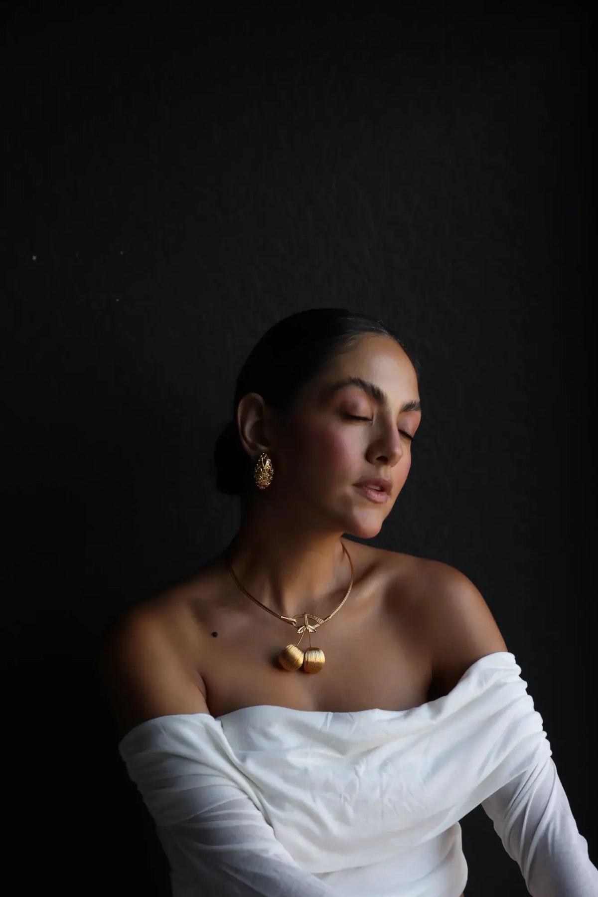 Gold tone cherry collar necklace worn with an off-shoulder white top