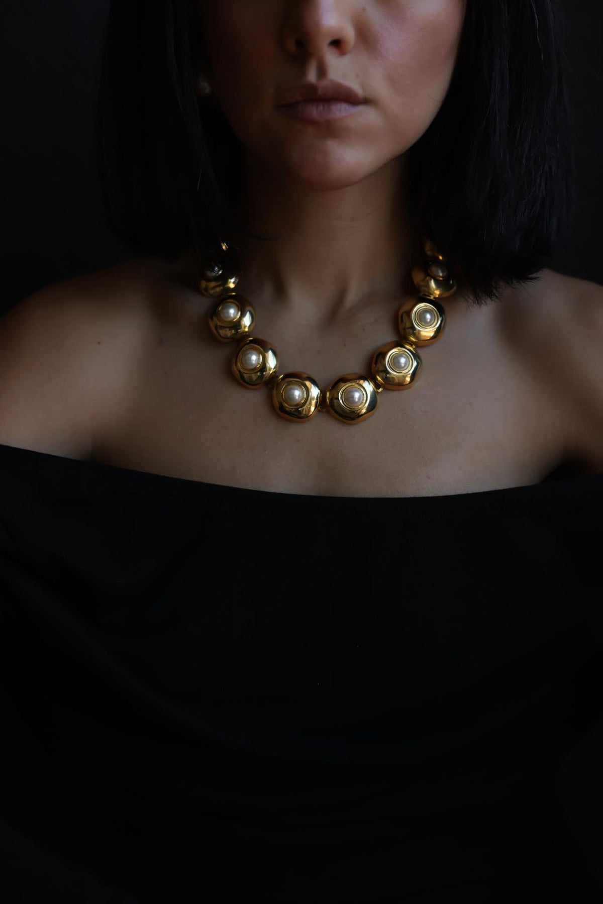 Gold tone faux pearl link collar necklace worn with an off-shoulder black top