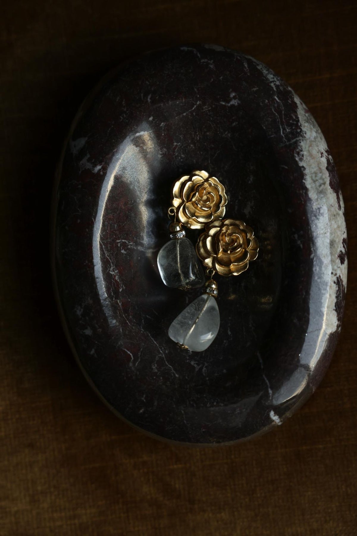 Gold plated rose clear stone drop clip-on earrings on a marble dish